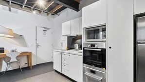 A modern kitchen with white cabinetry, a built-in oven, microwave, and a stainless steel refrigerator.