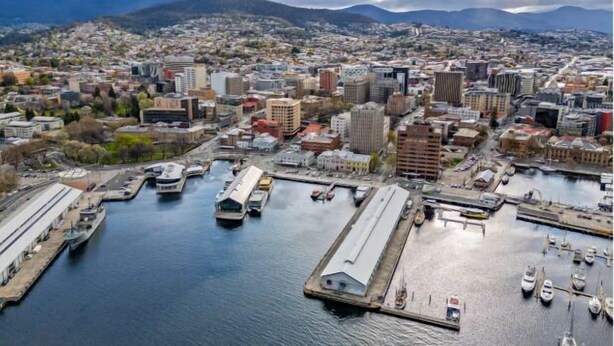 Une vue urbaine avec un port de plaisance, des bateaux et des montagnes en arrière-plan.