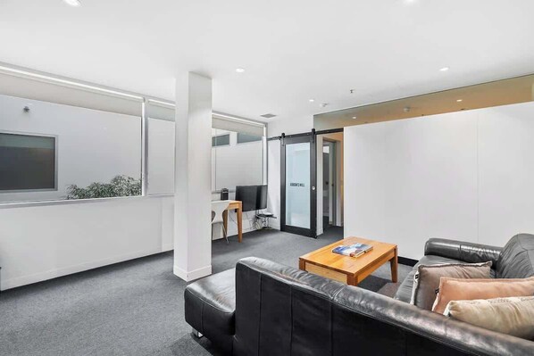 Un espace de bureau moderne avec un canapé en cuir, une table basse en bois et un téléviseur fixé à un mur blanc.