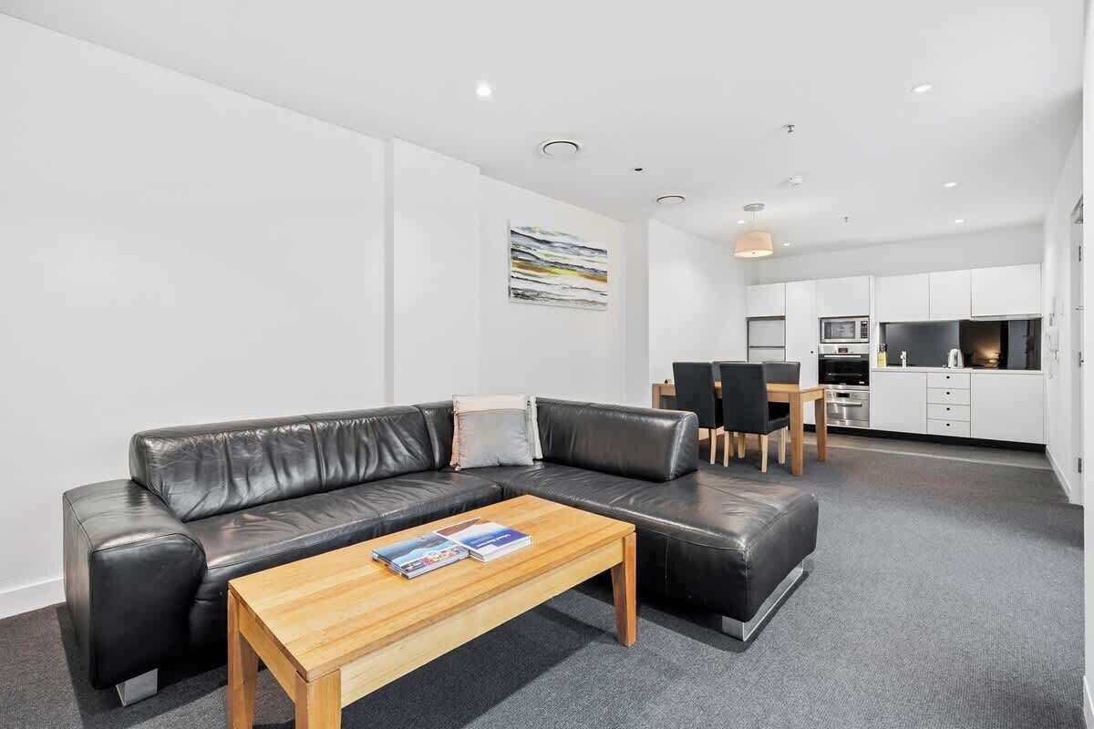 A modern living room with a black leather sofa, a wooden coffee table, and a dining area with a table and chairs.