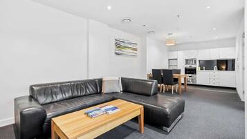 A modern living room with a black leather sofa, a wooden coffee table, and a dining area with a table and chairs.