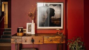 Una habitación con pared roja, una consola de madera, un cuadro enmarcado, una lámpara colgante y una planta en maceta.