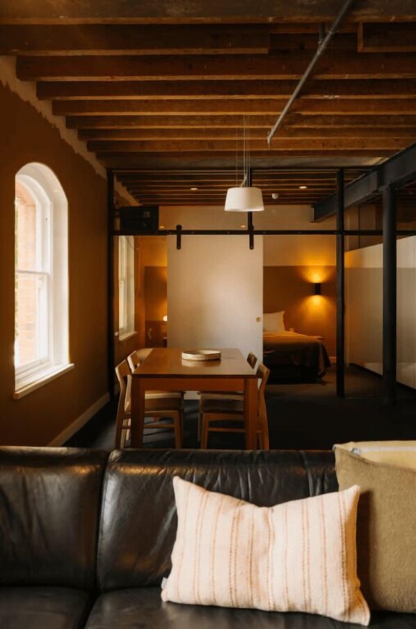 A cozy room with a wooden ceiling, a dining table with chairs, a sofa with cushions, and a bed with a headboard.