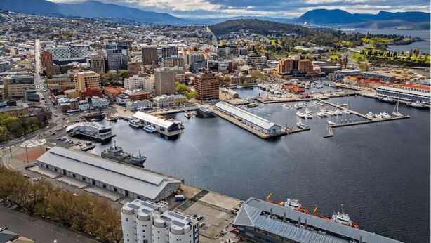 Vista aérea de una ciudad con un puerto deportivo, edificios y montañas al fondo.