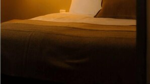 Habitación de hotel con cama, mesita de noche y lámpara de pared.