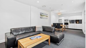 A modern living room with a black leather sofa, a wooden coffee table, and a dining area with a table and chairs. - Gibson's Mill 1 Bedroom Warehouse Apartment with Atrium
View - 204 (Hobart)