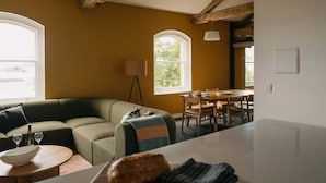 A cozy living room with a green sofa, a dining table, and a lamp. - Gibson's Mill 3 Bedroom Loft Penthouse with Private
Balcony&Waterfront Views-301 (Hobart)