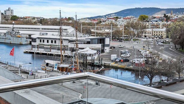A marina with boats docked, a large building with a white facade, and a view of a cityscape with buildings and hills in the background.