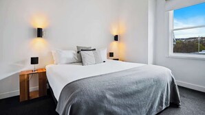 A modern hotel room with a large bed, two bedside tables, and wall-mounted lighting.