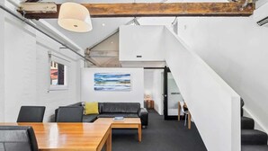 Un espacio de oficina moderno con una mesa de madera, un sofá de cuero negro y una escalera que conduce a otro nivel.
