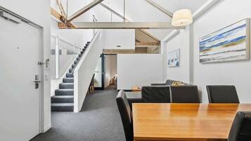 A modern interior with a staircase, a dining area with a wooden table and black chairs, and a painting on the wall.