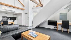 Et moderne interiør med en sort lædersofa, et træbord, et skrivebord med en computer og et køkkenområde.