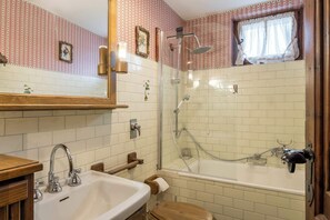 Features a large mirror, a sink with a countertop, a glass-enclosed shower with a handheld showerhead, and a small window.