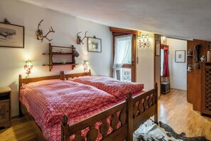 Cozy bedroom with a double bed, nightstand, and wooden cabinet, featuring decorative items and a window with a white curtain.
