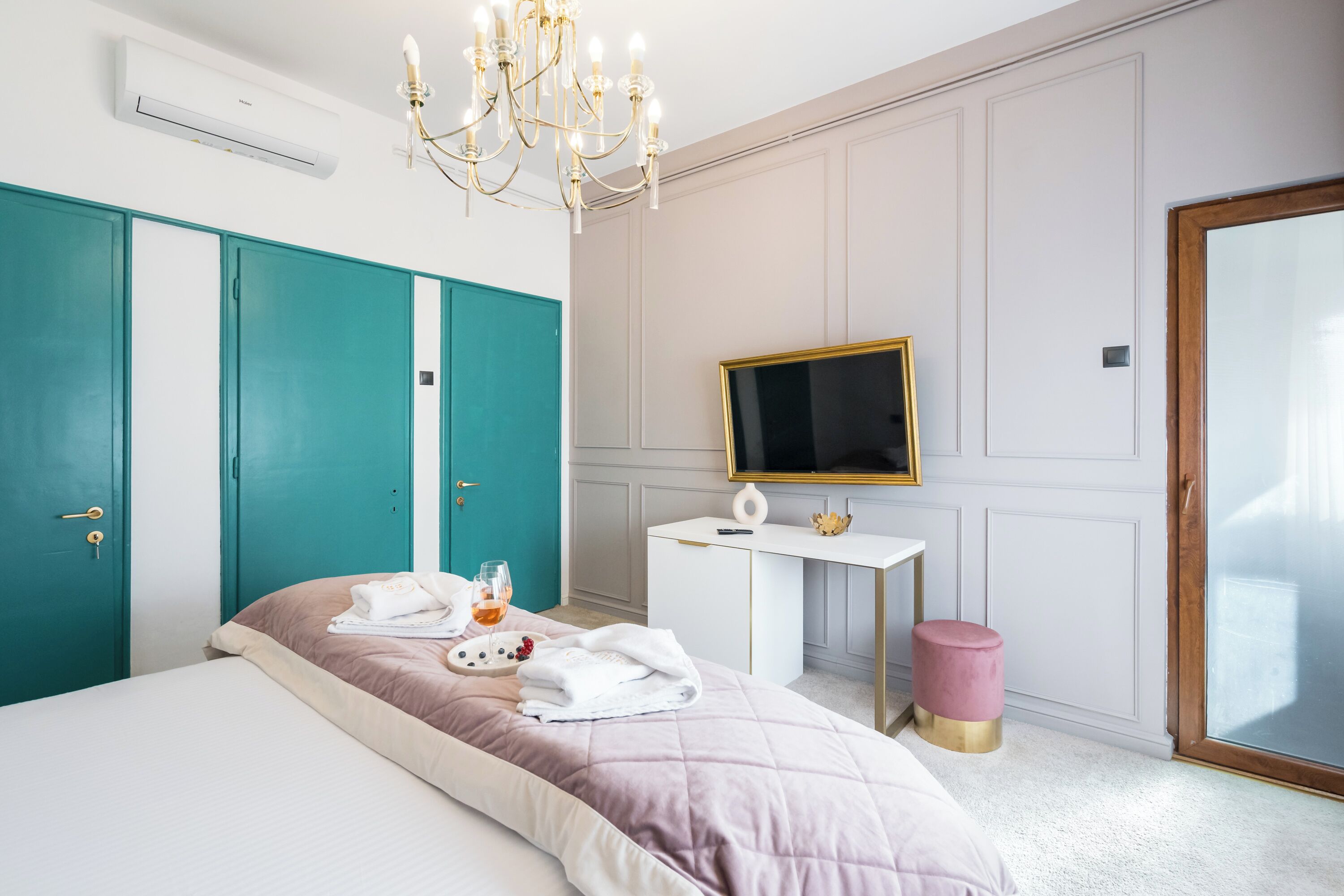 Un dormitorio con cama, escritorio, televisión y puertas color esmeralda.