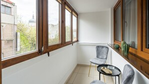 Una habitación pequeña y luminosa con ventanas amplias, pared blanca y suelo de baldosas.