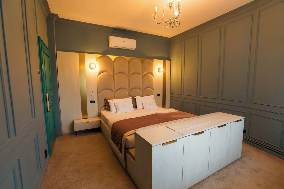 Quarto com cama, mesas de cabeceira, cômoda e lustre.