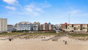A coastal hotel with multiple floors, balconies, and a sandy beach area in front.