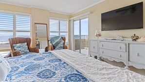 A bedroom with a large bed, a television, a dresser, and a view of the ocean.