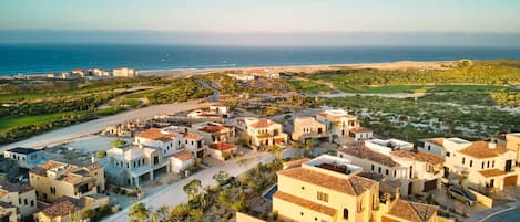 A coastal residential area with houses featuring Mediterranean architecture, a road, and a view of the ocean.