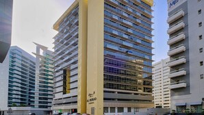 Un immeuble moderne de grande hauteur, doté de nombreux balcons et d’une façade jaune très visible.