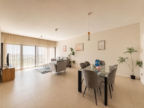 A modern living room with a sofa, dining table, chairs, a TV, and artwork on the walls. - Minissy Suites (Moka)