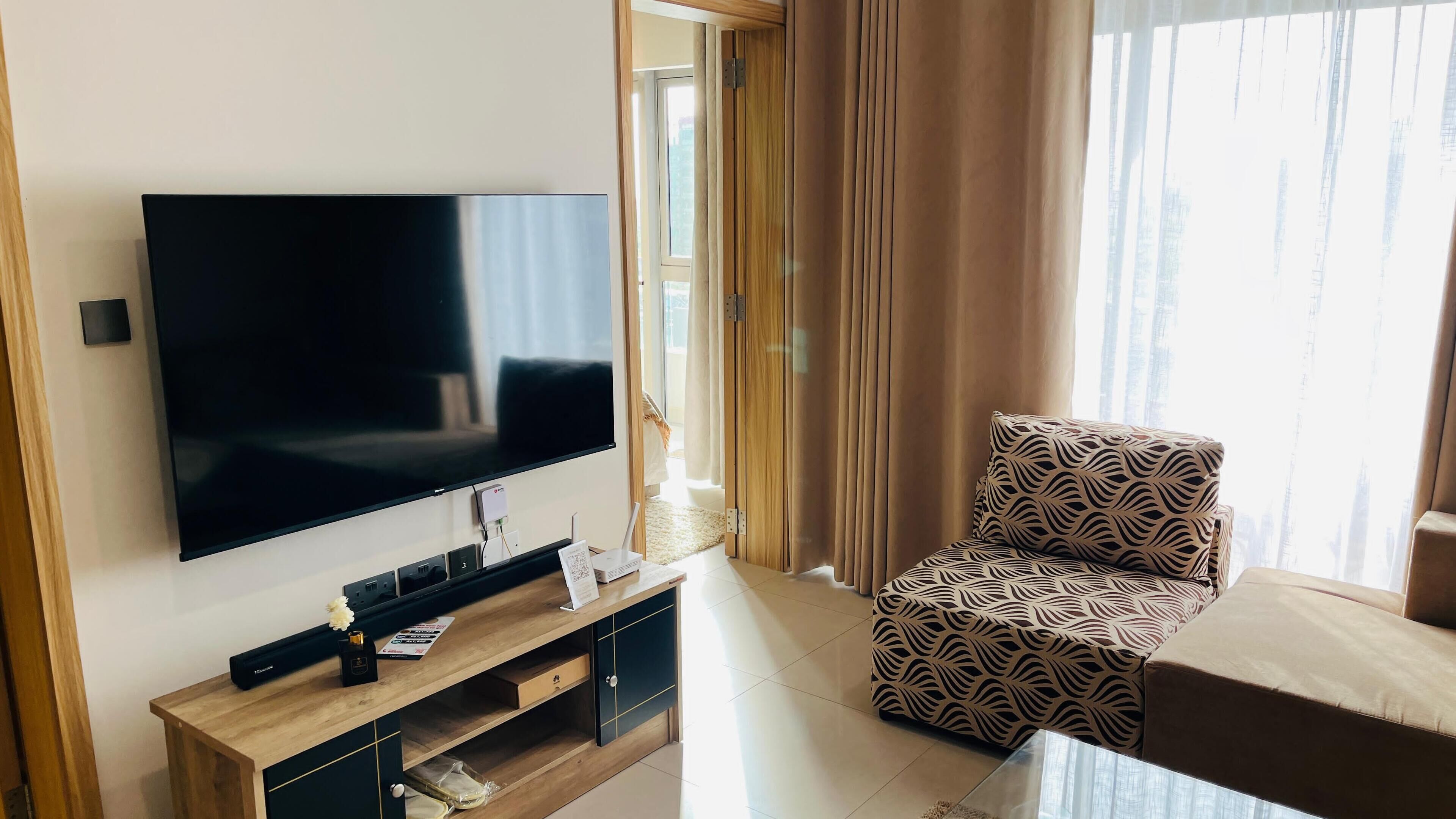 Ein modernes Wohnzimmer mit Flachbildfernseher, einer Holzunterhaltungsecke, einem gemusterten Sessel und einem Sofa.