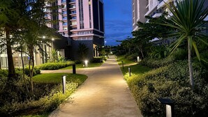 Un chemin bien éclairé dans un quartier résidentiel, bordé de bâtiments modernes et d’une végétation luxuriante.