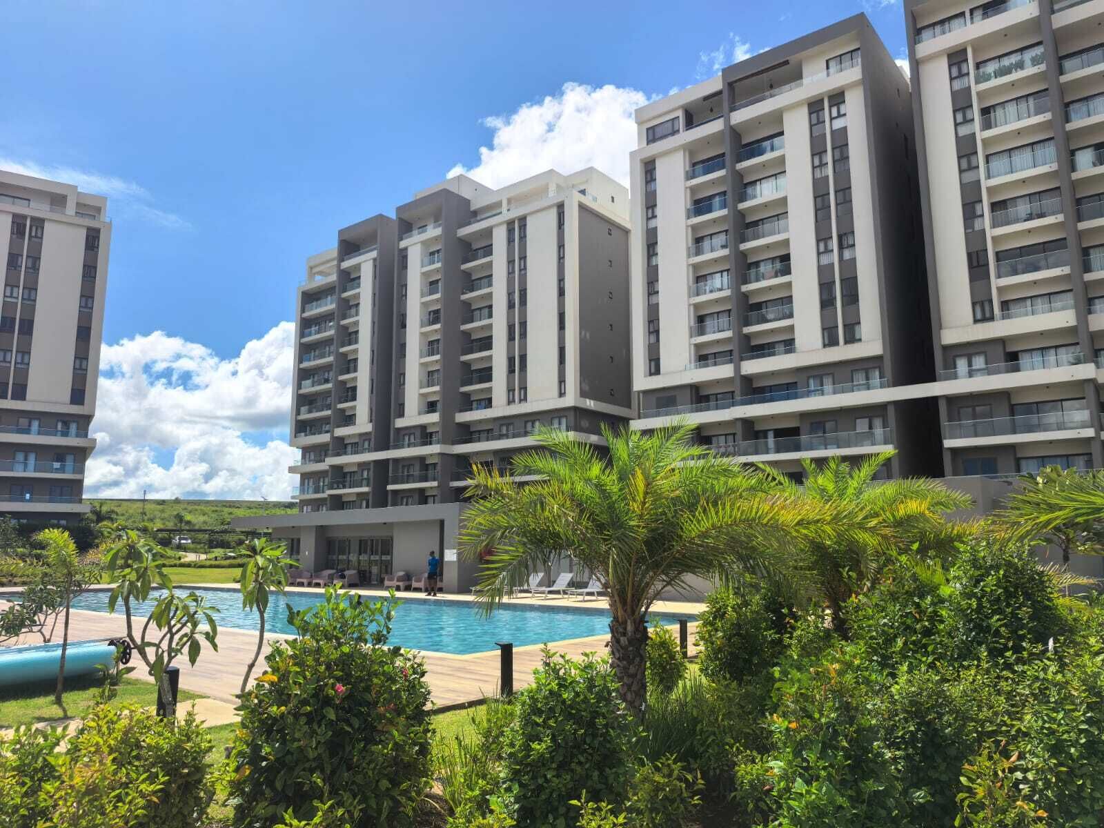 A modern apartment building with multiple balconies, a swimming pool, and lush greenery.