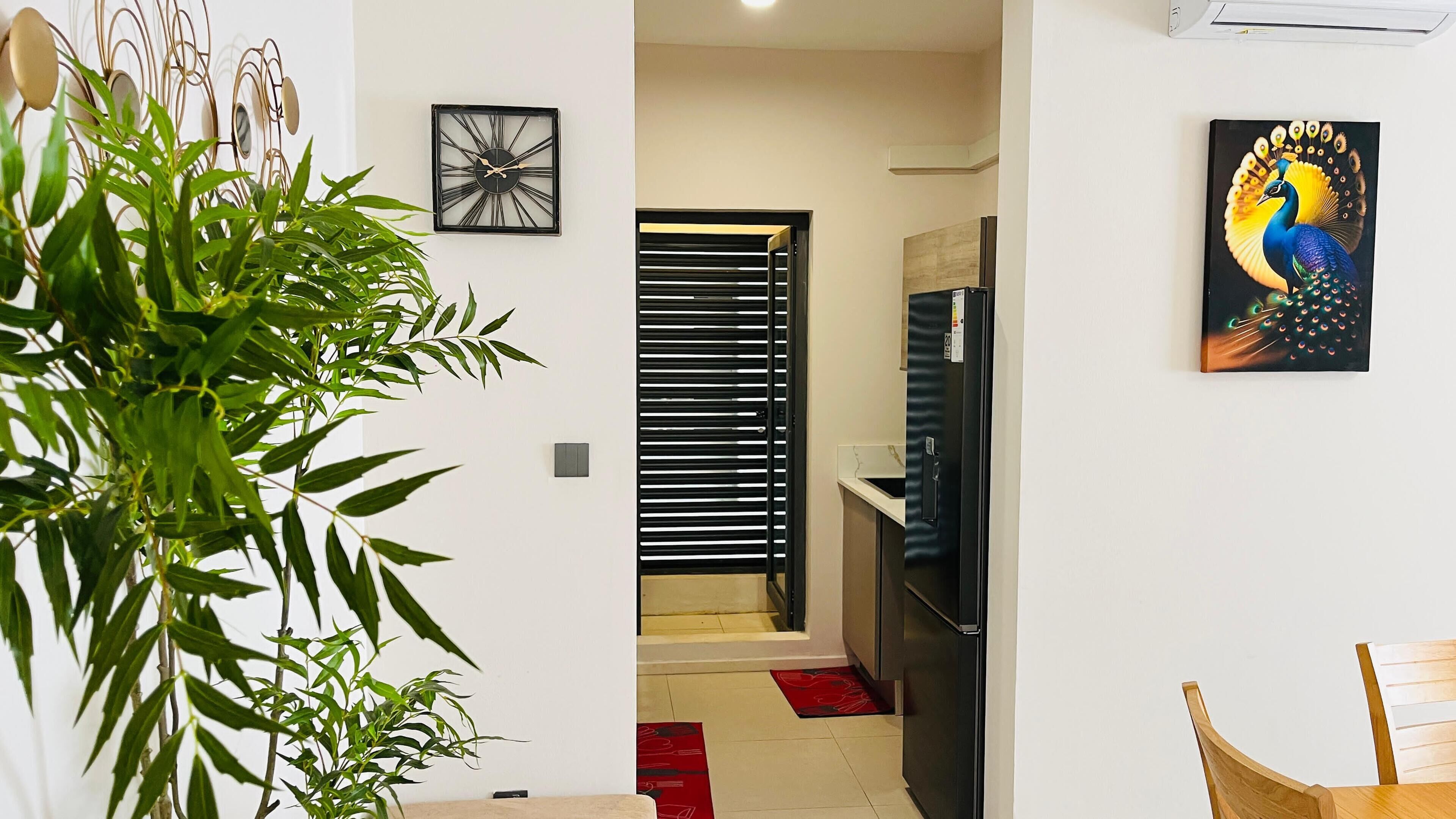 Un pasillo con una planta, un reloj, una puerta y un refrigerador.