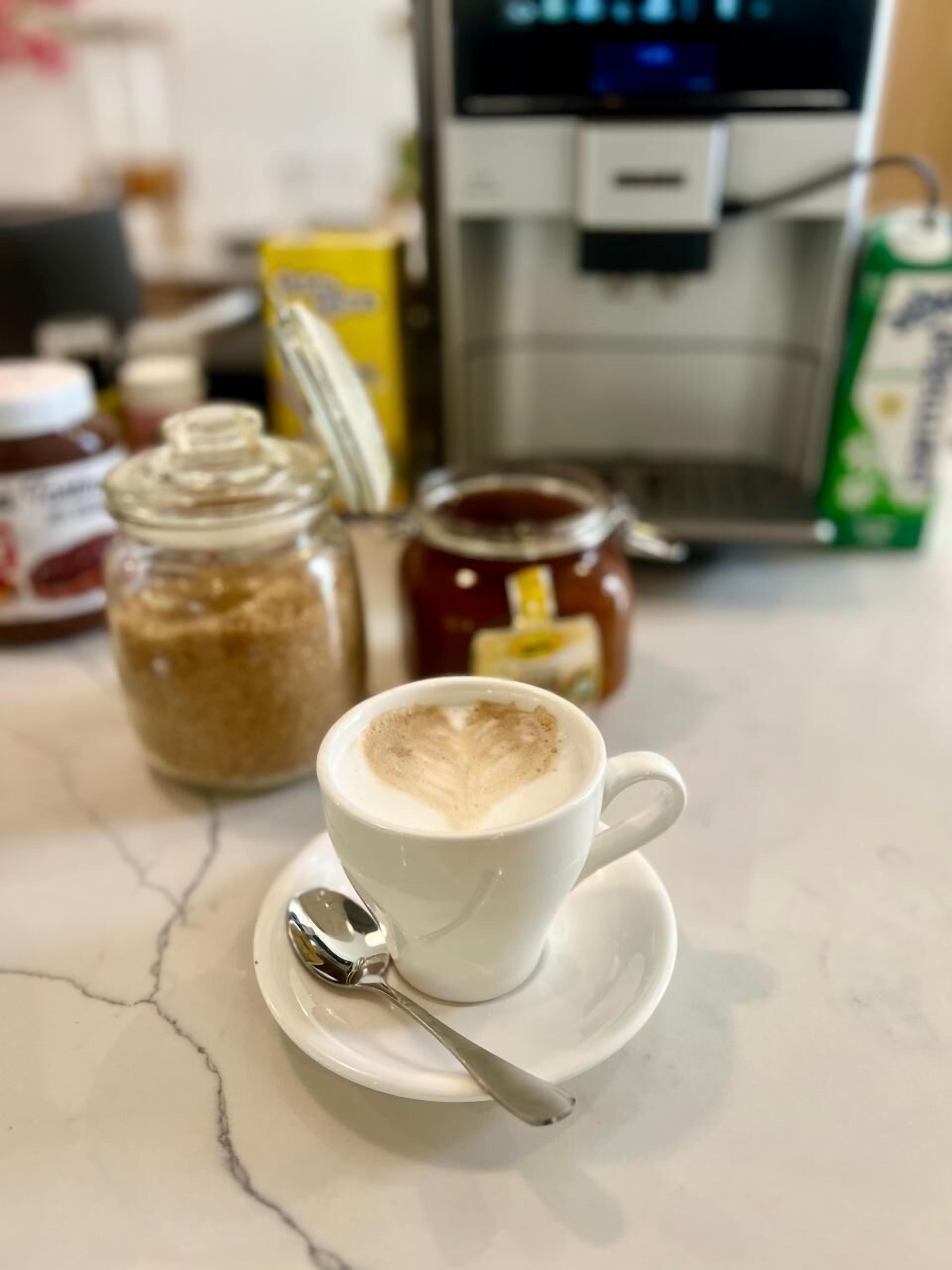Une tasse de café avec une cuillère sur une soucoupe, un pot de miel et un pot de confiture sur un plan de travail en marbre.