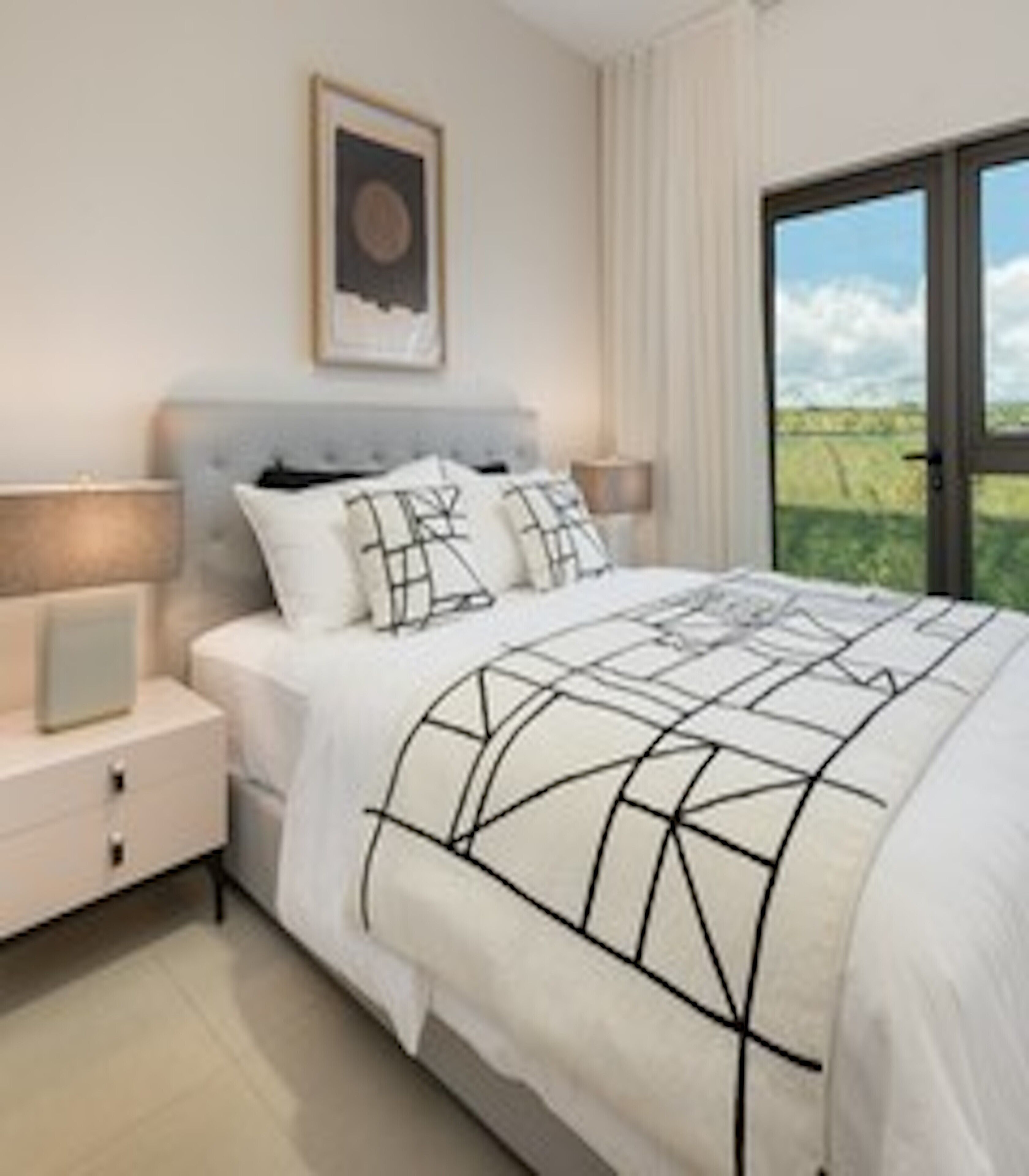 A bedroom with a bed, nightstands, a lamp, a framed picture on the wall, and a view through a window.