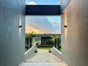 Une entrée moderne, avec un chemin en béton menant à une porte en verre, le tout entouré de verdure et sous un ciel dégagé.