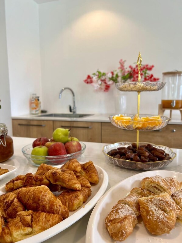 A breakfast setting with croissants, fruits, and a honey dipper.