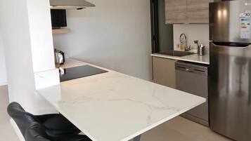 Ett modernt kök med en vit marmorskiva, rostfria köksmaskiner och en svart stol.