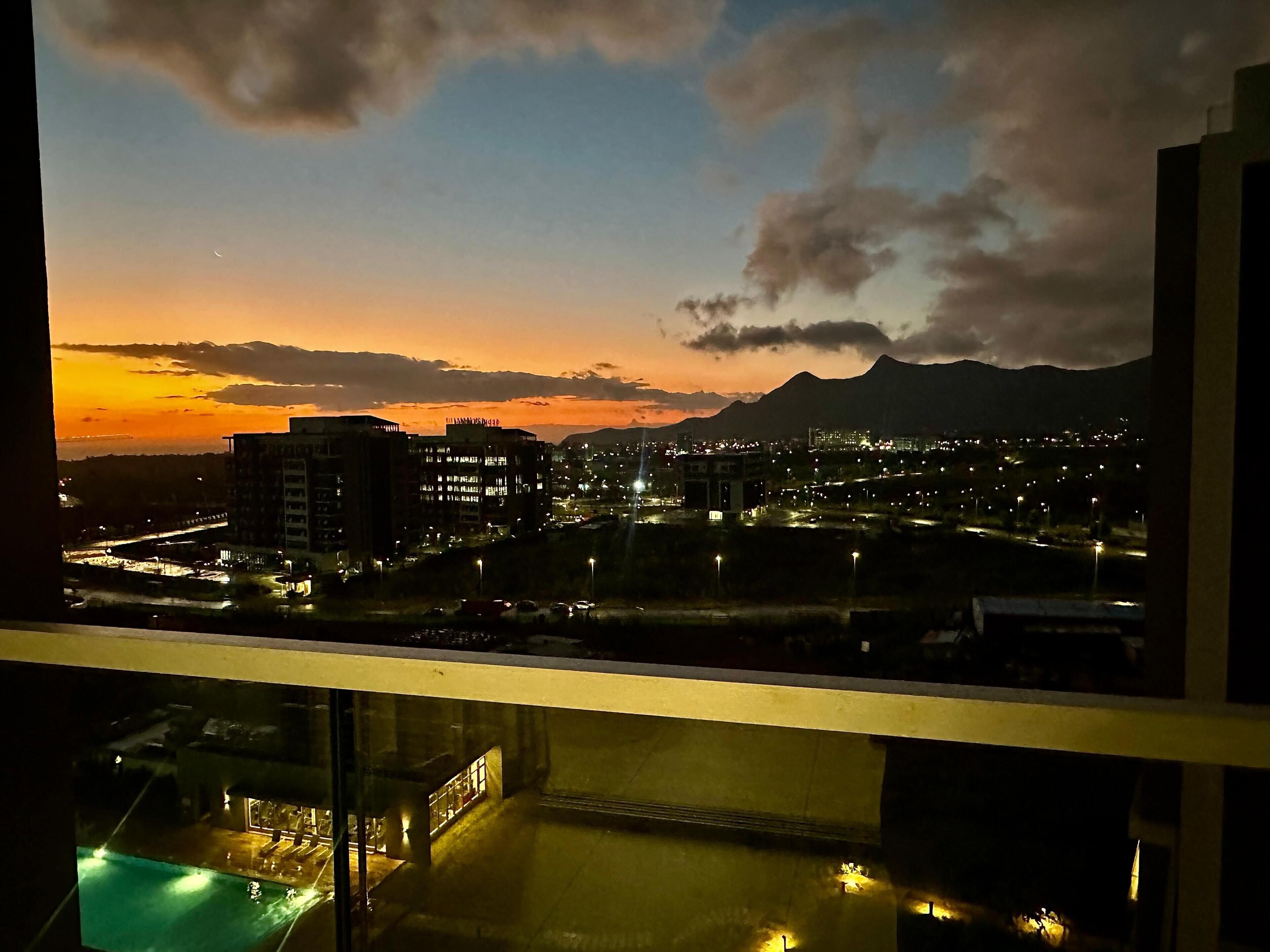 A cityscape at dusk with illuminated buildings and a mountain in the background.