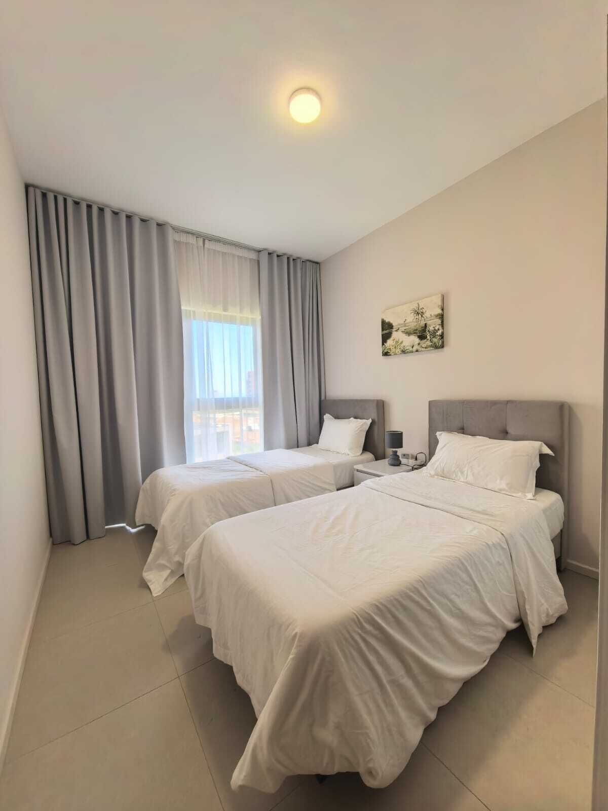Habitación de hotel con dos camas, un ventanal con cortinas, una lámpara en el techo y un cuadro colgado en la pared.
