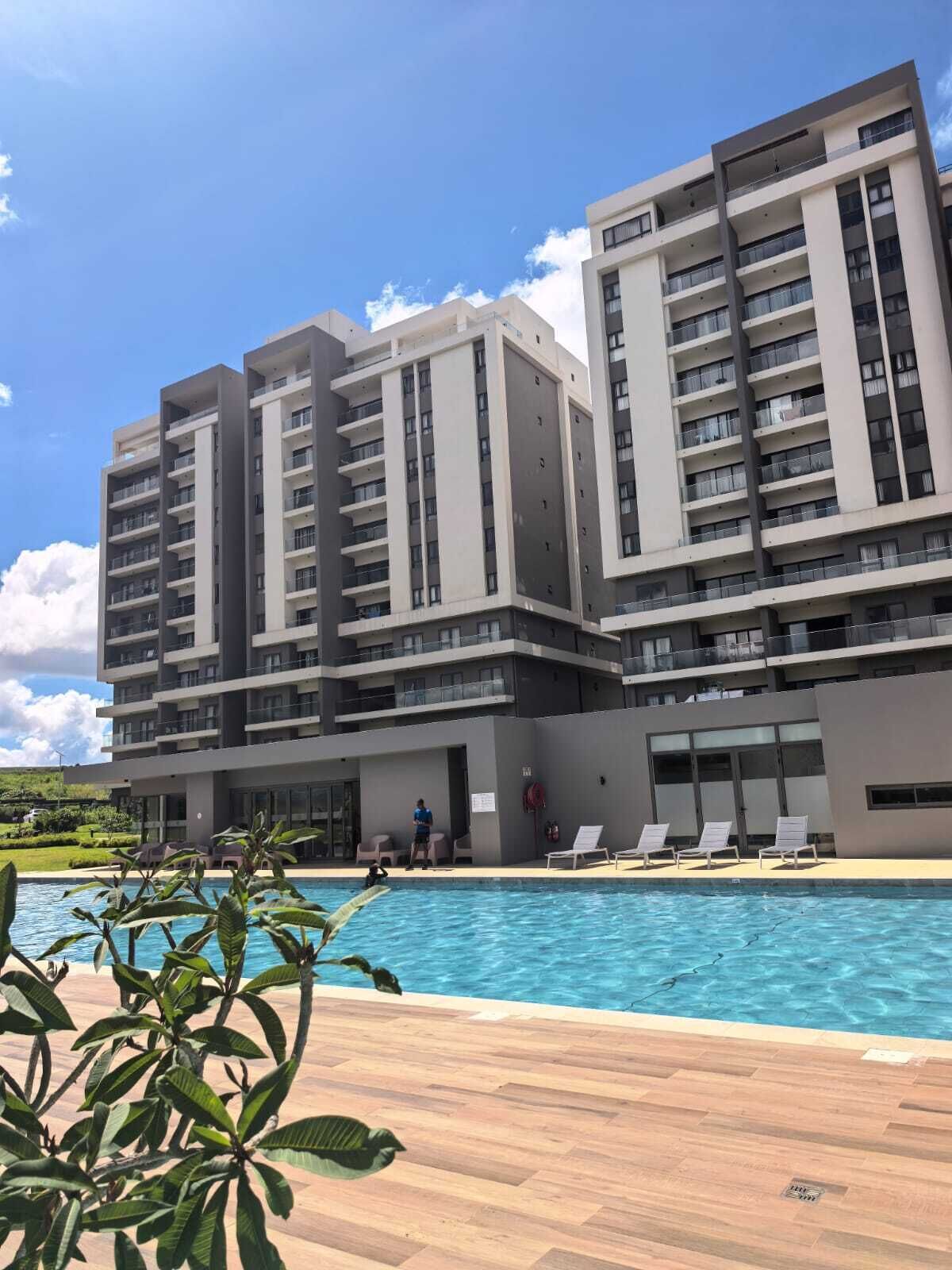 A modern hotel with multiple floors, a swimming pool, and a landscaped area with plants.
