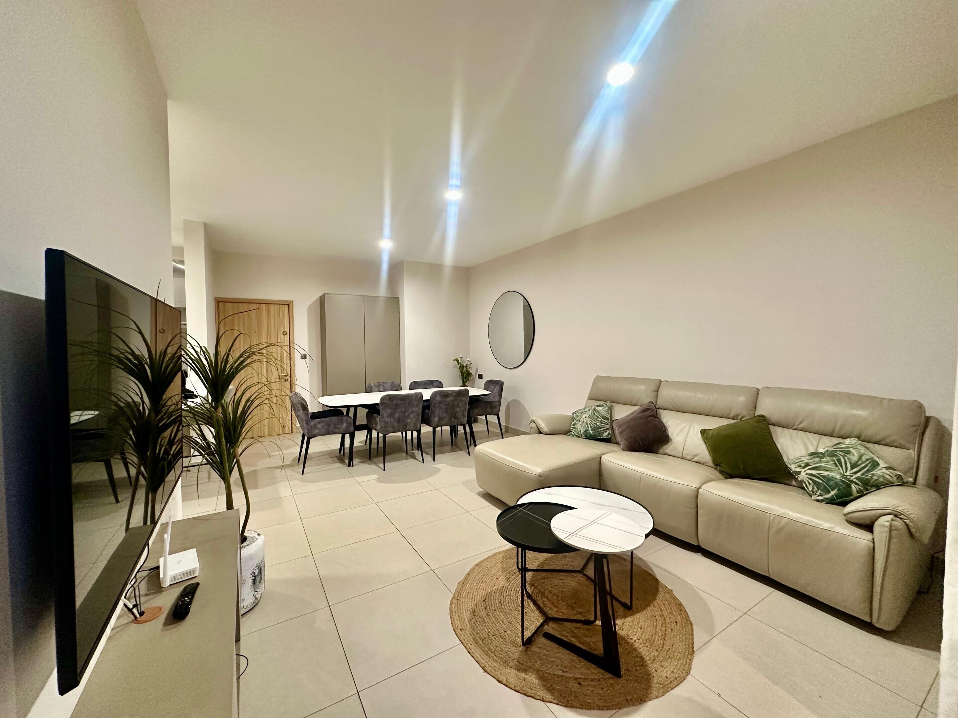 Ein modernes Wohnzimmer mit Sofa, Couchtisch, Fernseher und Essbereich mit Stühlen und Tisch.