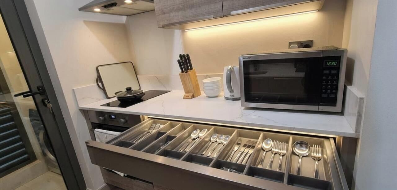 A kitchen with a microwave, utensils drawer, and a small countertop with a knife block and a bowl.
