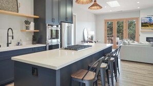 A modern kitchen with dark cabinets, a large island, and pendant lighting. - The Vineyard Estate at Paradise Ridge by Kohmsa (Santa Rosa)