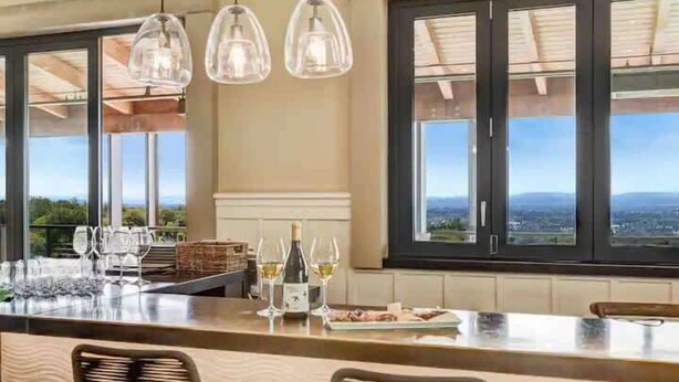 A dining area with a bar, large windows, and hanging pendant lights. - The Vineyard Estate at Paradise Ridge by Kohmsa (Santa Rosa)