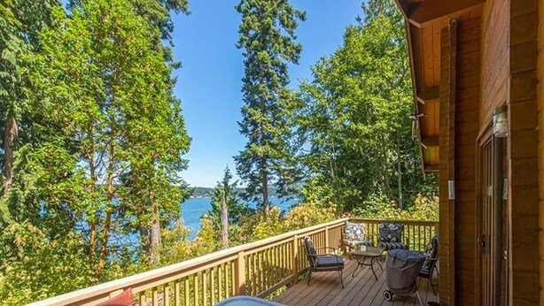 A wooden deck with a hot tub, outdoor seating, and a view of the sea. - Waterfront, Rustic, Hot Tub, Pet-Friendly (Sequim)