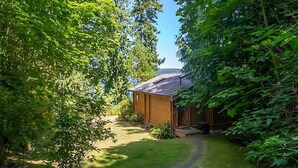 A wooden cabin surrounded by lush greenery and a clear sky. - Waterfront, Rustic, Hot Tub, Pet-Friendly (Sequim)