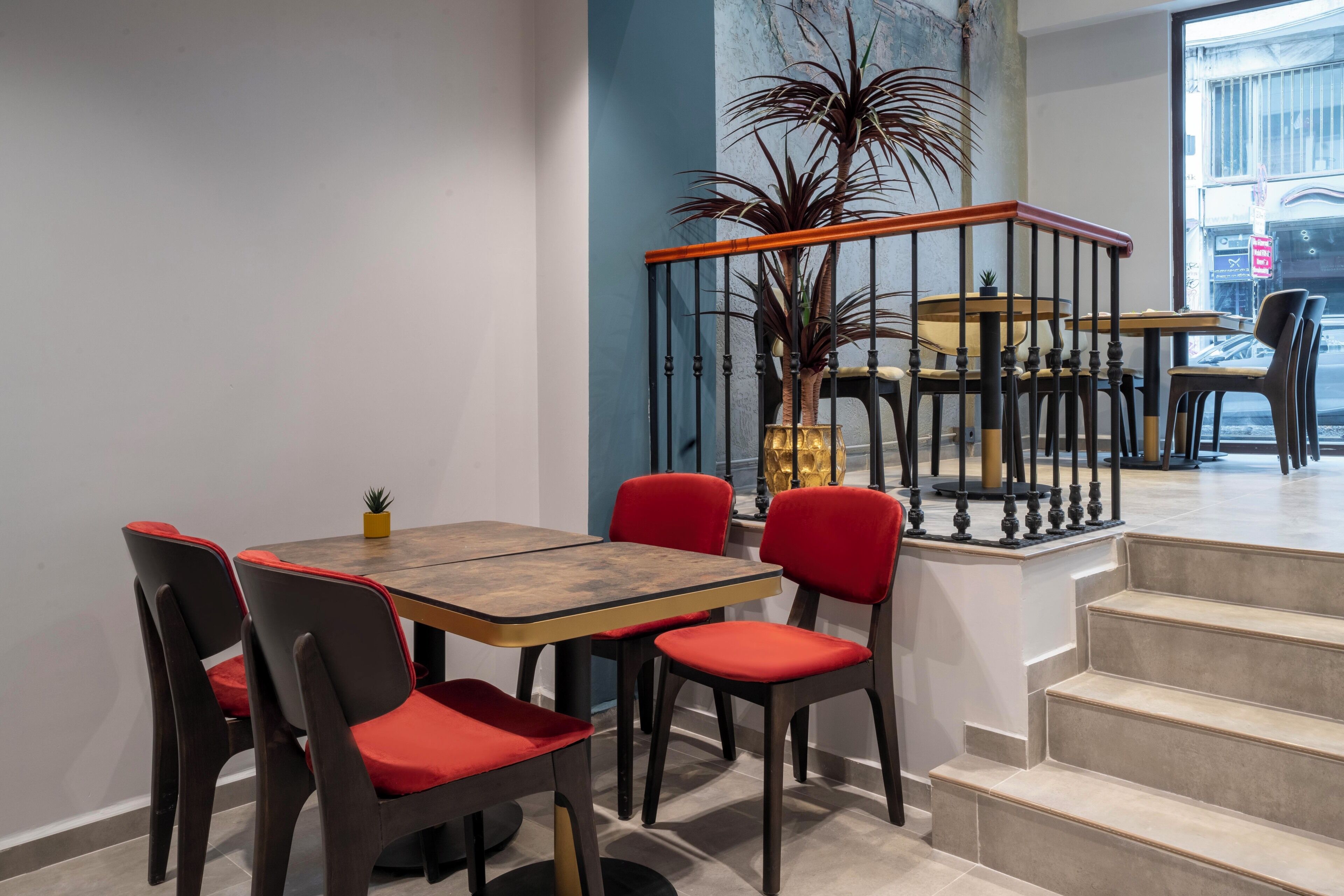 A dining area with a wooden table and red chairs, a staircase, and a view of the street.