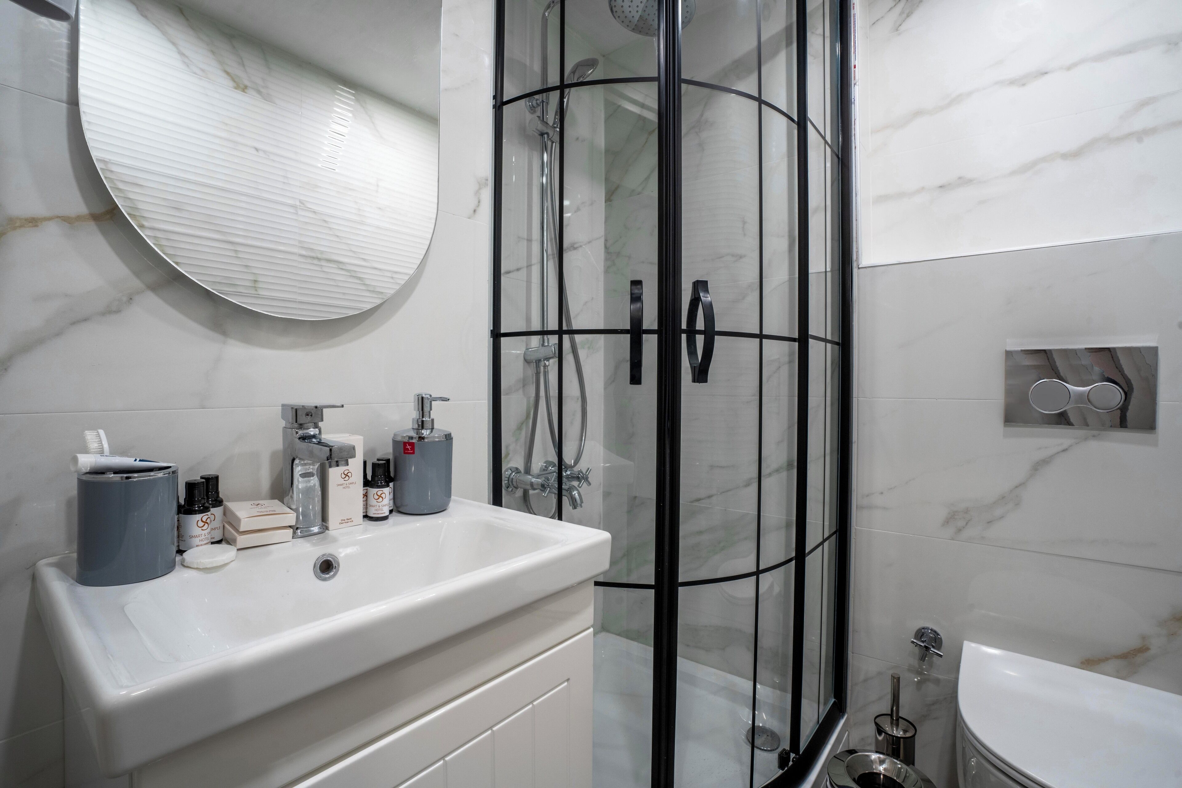 Une salle de bain moderne avec un lavabo blanc, une douche à l’italienne et un miroir rond.