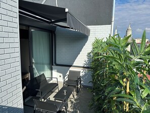 A patio with a table and chairs, a covered seating area, and a view of a building with a brick facade and a window.