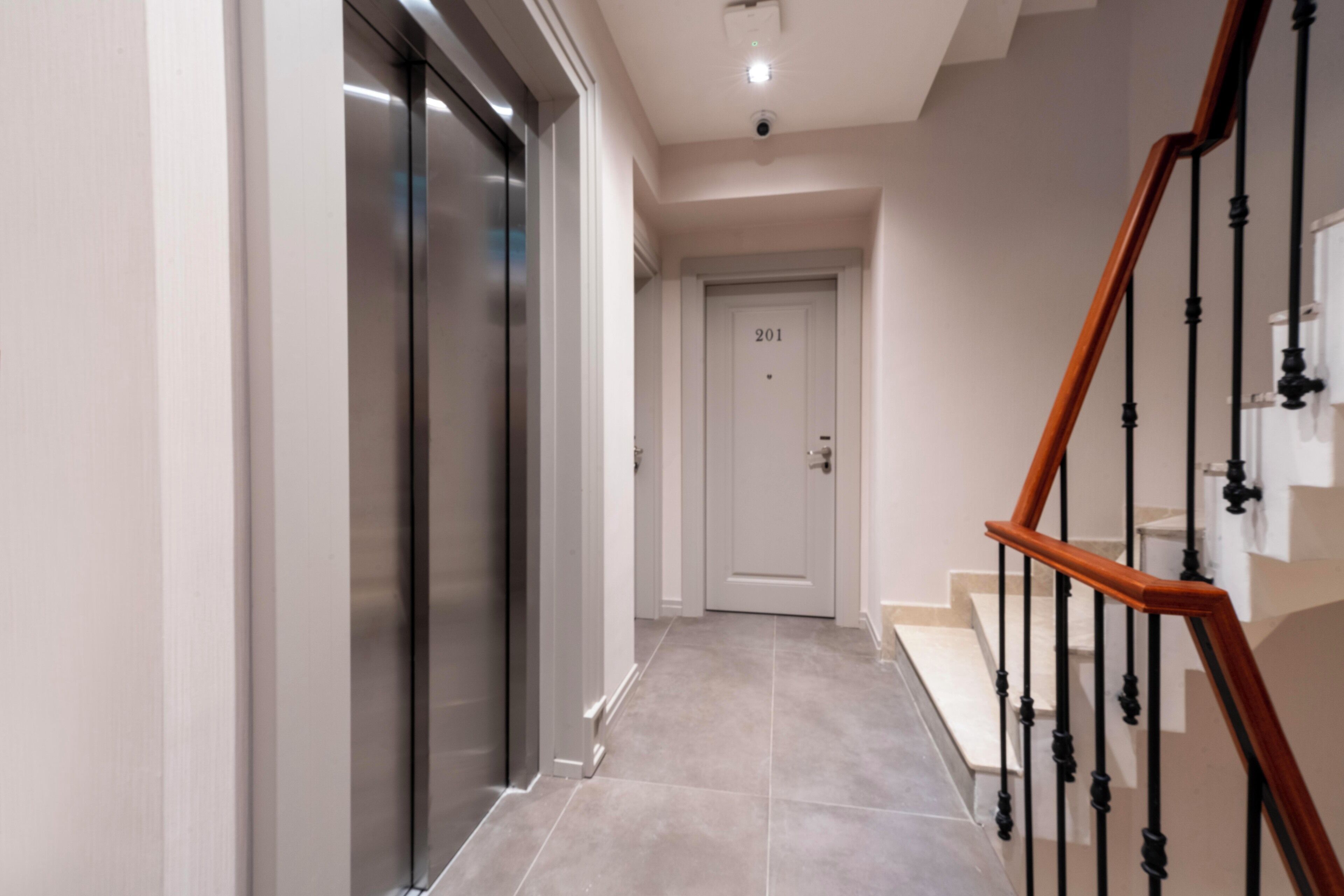 A modern hallway with a glass elevator, a wooden staircase, and a door marked "201".