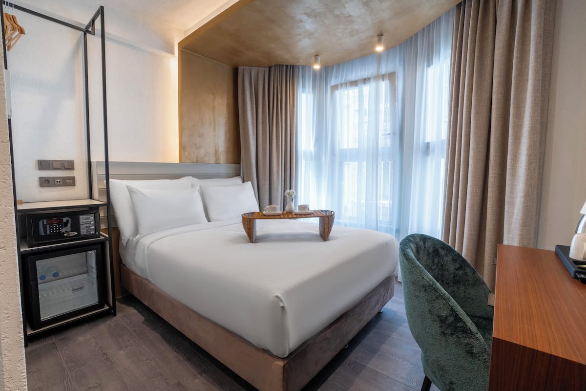 A hotel room with a large bed, a bedside table, a chair, and a desk.