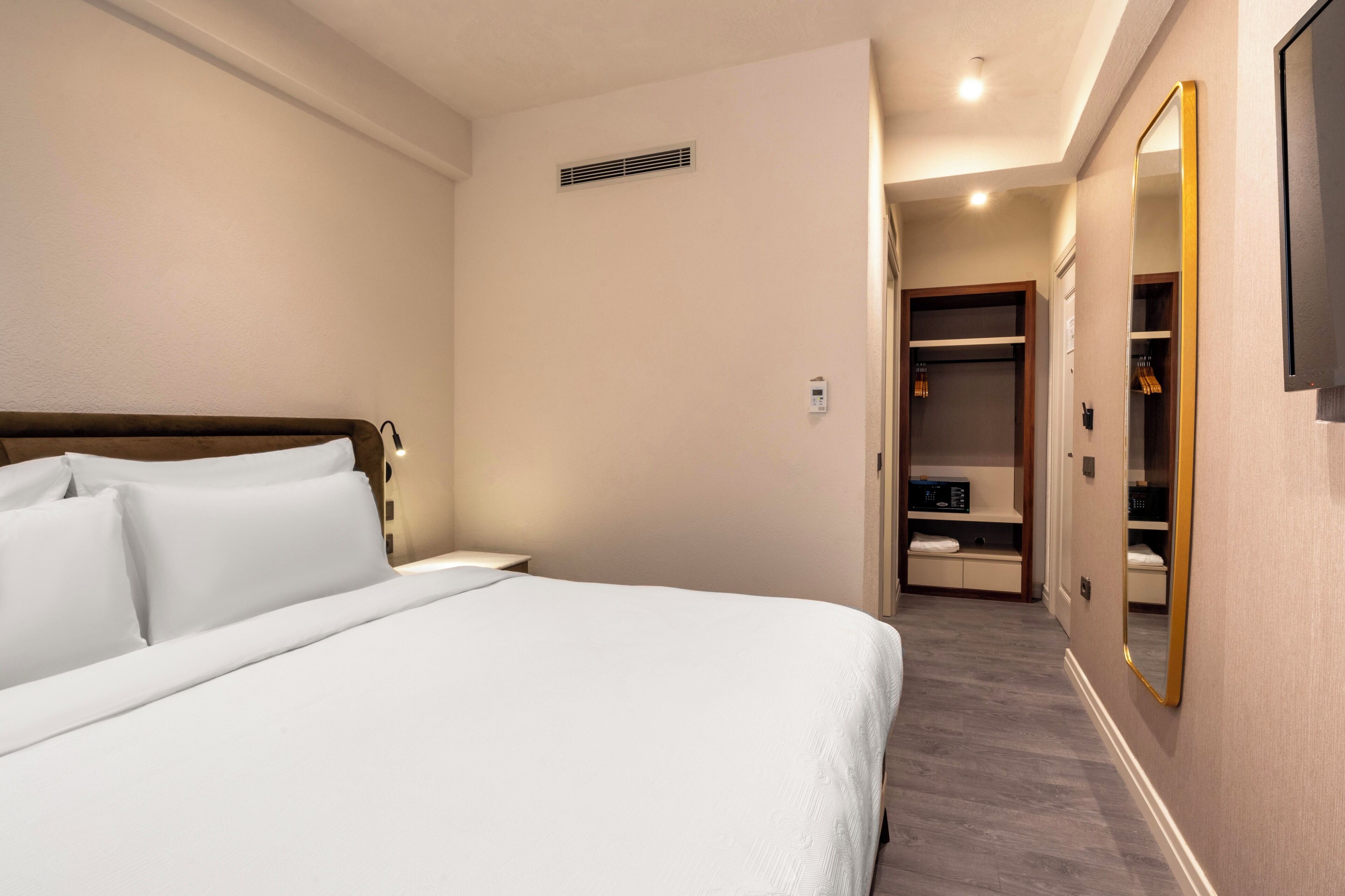 Une chambre d’hôtel avec un lit bien fait, un dressing et un miroir au mur.